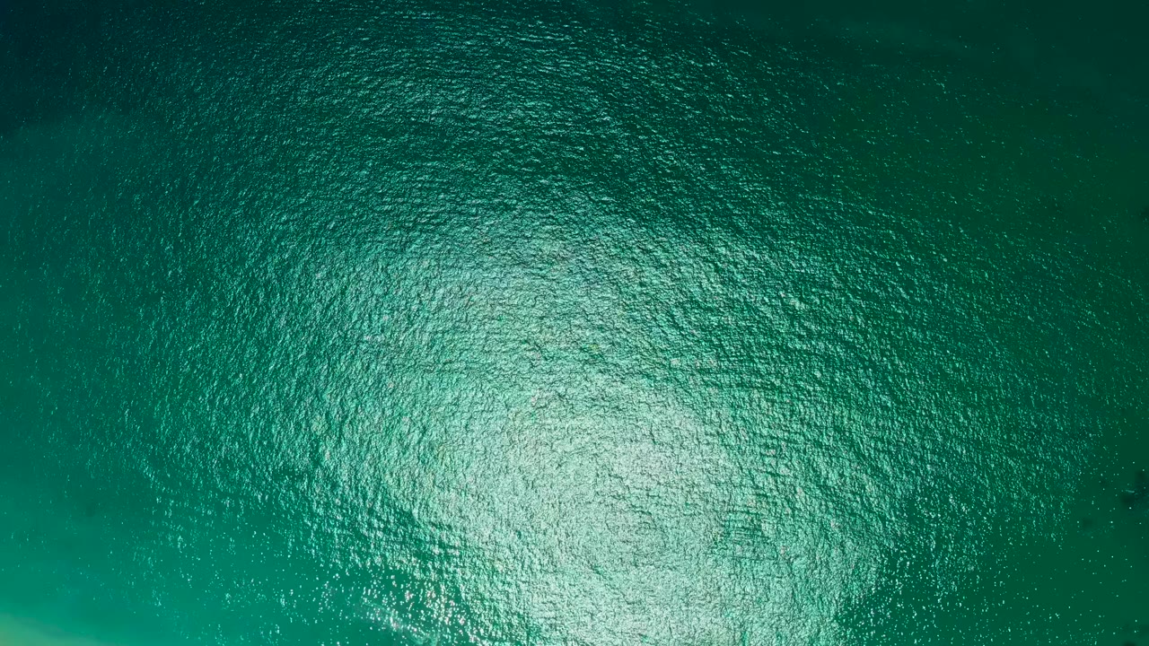Aerial overhead view of turquoise water at Marquis Los Cabos, Mexico, with dense small ripples, bright glare, and no visible people or shoreline.