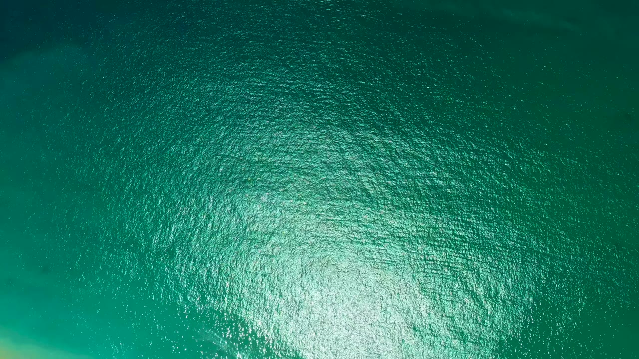Green-blue ocean surface at Marquis Los Cabos shows a broad reflective highlight near the bottom center, darker water toward the top, and no visible people.