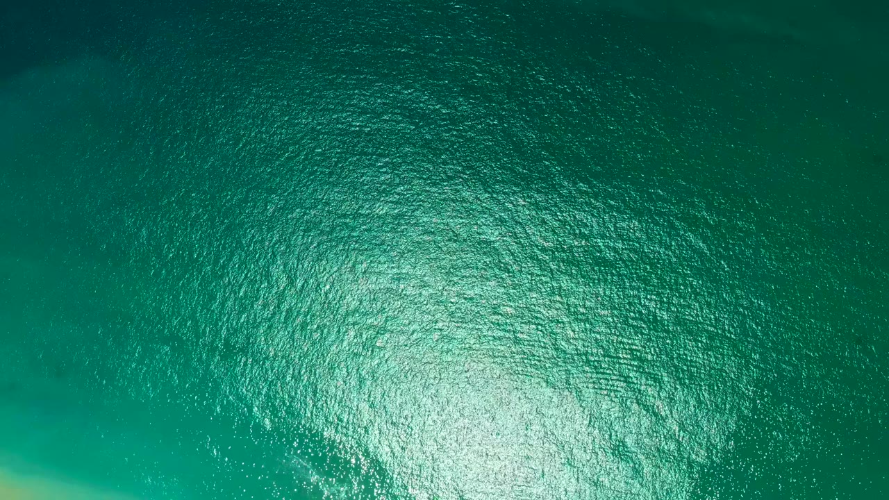 A teal ocean surface at Marquis Los Cabos fills the view with tight ripple texture, a strong sun glint low in frame, and no visible people or objects.