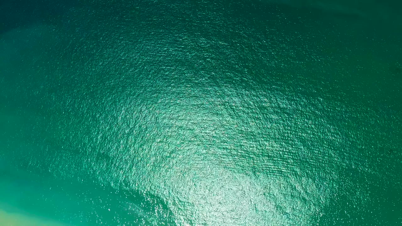 Ocean surface with bright shimmer near the lower edge and subtle turquoise banding.