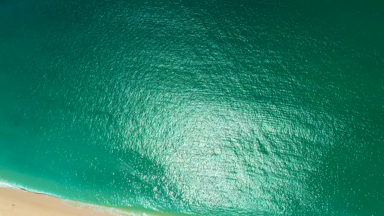Aerial turquoise water with wave foam approaching sand