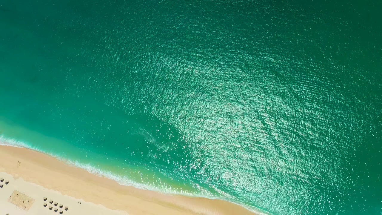 Aerial view over Marquis Los Cabos, Mexico, with the beach running diagonally along the lower left and turquoise water spreading across the frame, no visible people.