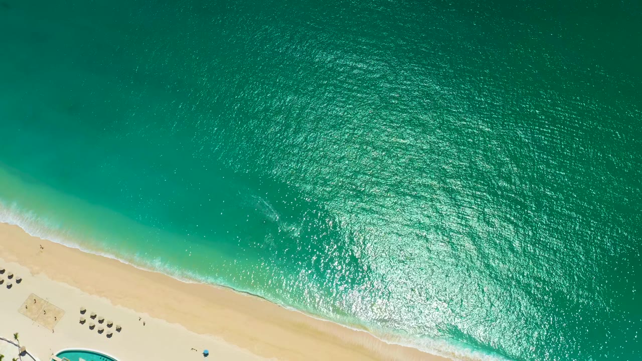 Overhead turquoise ocean beside pale sandy beach with small waves