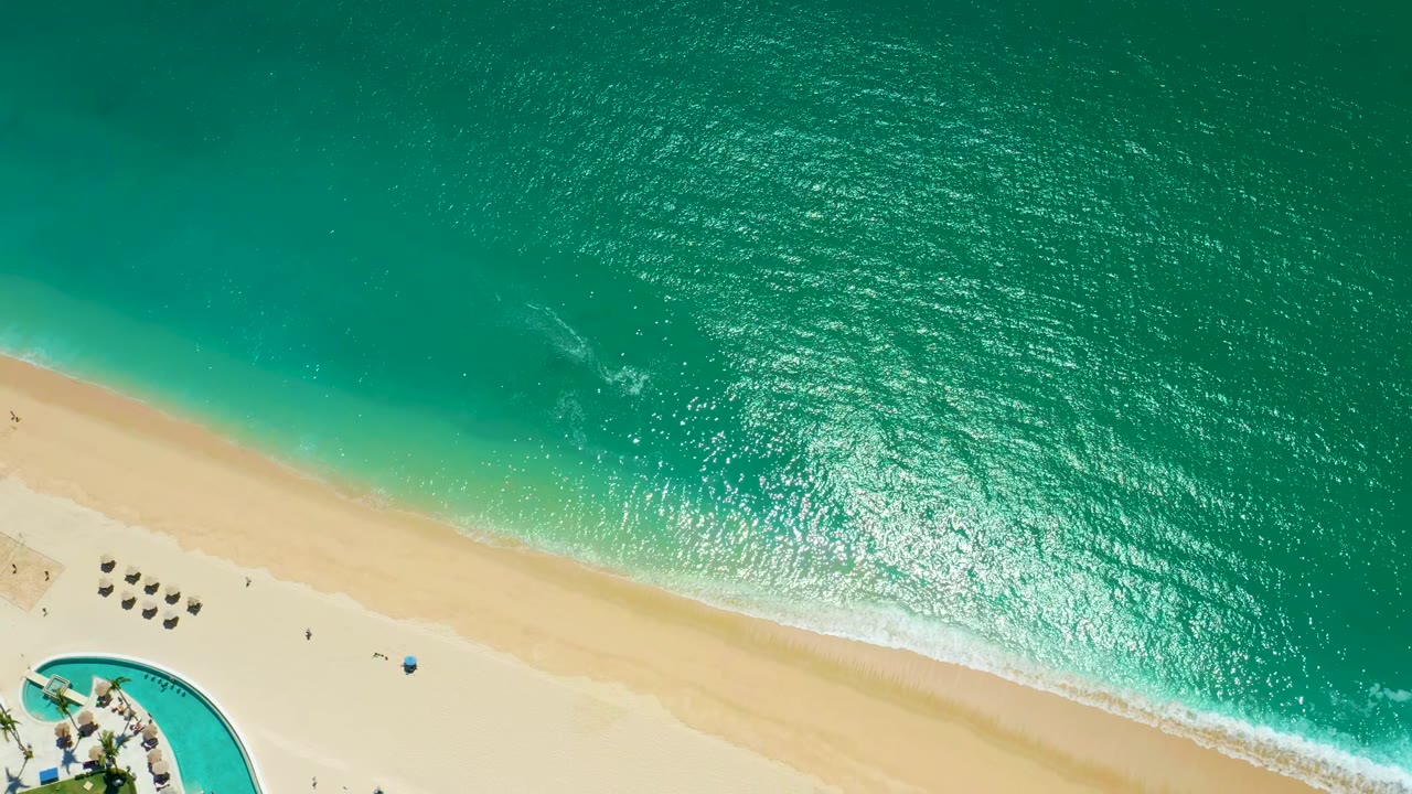 Aerial beach view with bright turquoise water and umbrellas on sand.