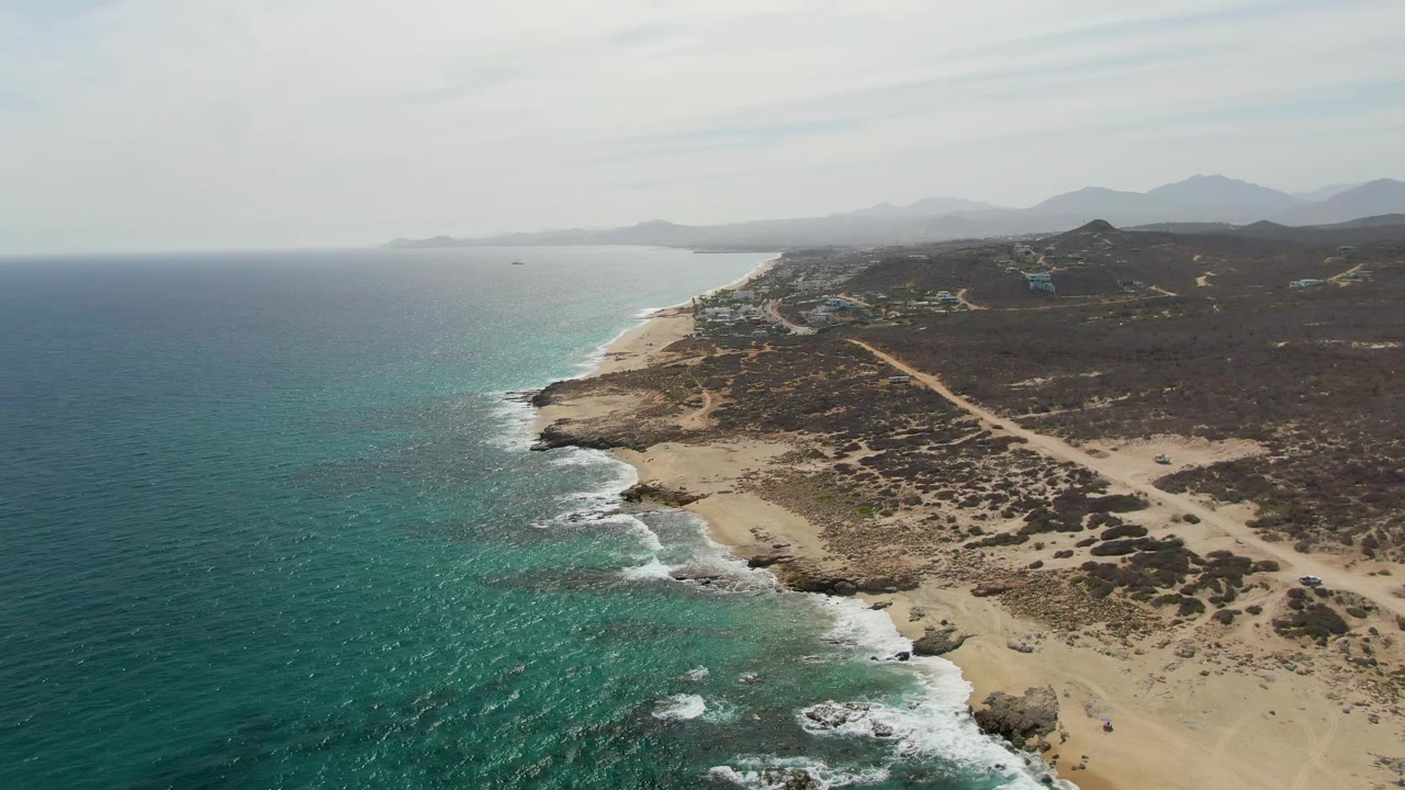 Aerial view of turquoise ocean waves along a rocky sandy shore.
