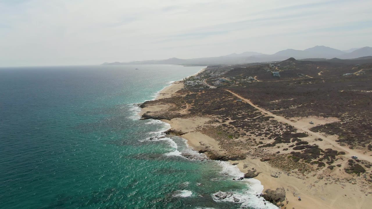 Drone view at Punta Gorda Beach with deep blue water shifting to turquoise near the rocky coast, sandy patches inland, and no visible people.