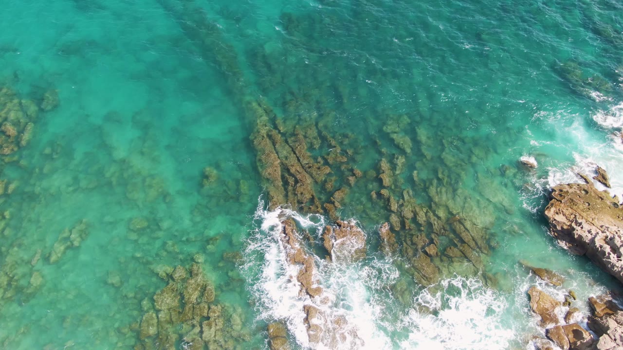 Turquoise ocean water over rocks with waves breaking near the lower edge.