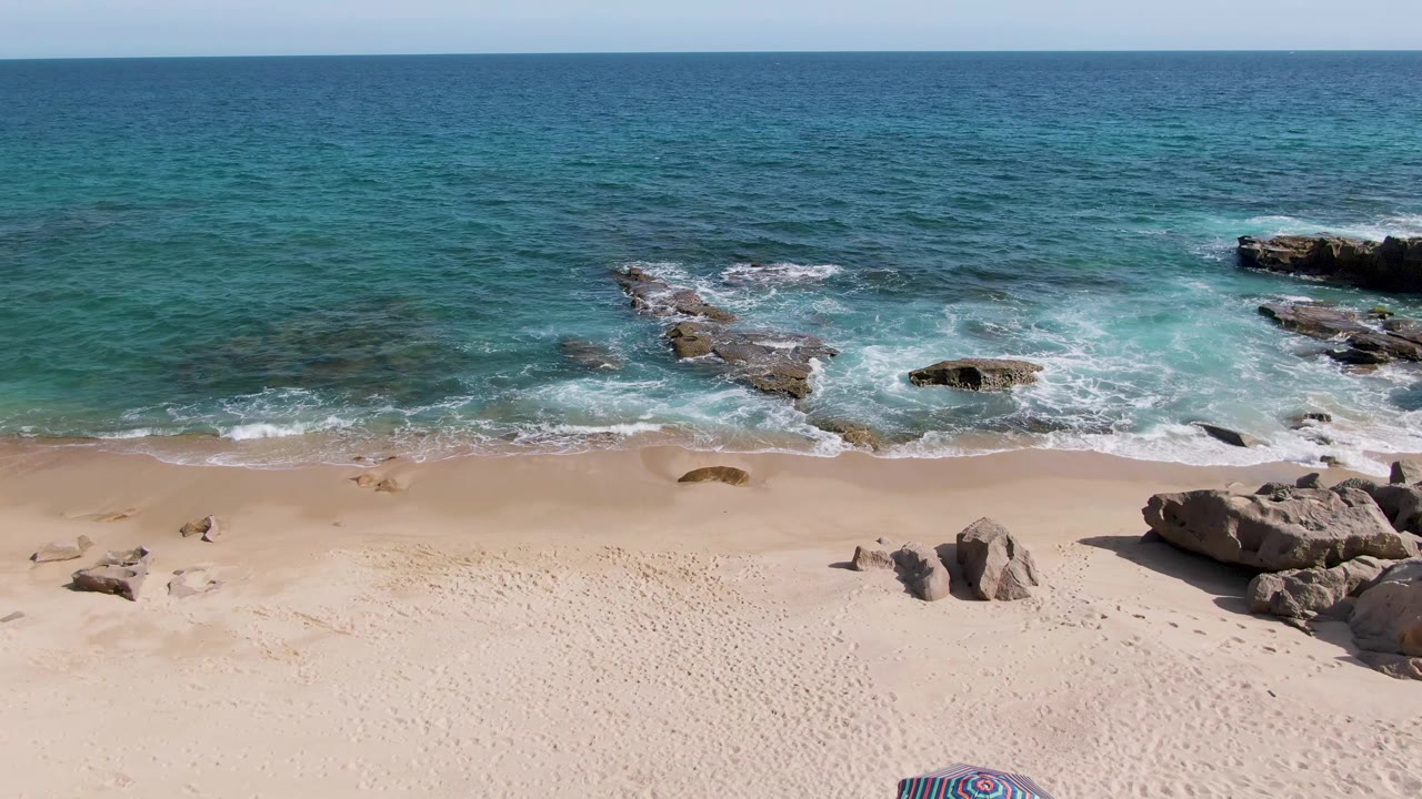 Rocky shoreline with waves washing onto a sandy beach.