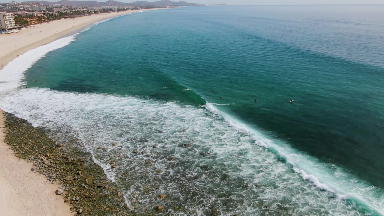 Aerial frame from Punta Gorda Beach, Baja California Sur, with a thicker band of white foam pushing over the rocky shallows and turquoise water beyond, with no discernible people visible.
