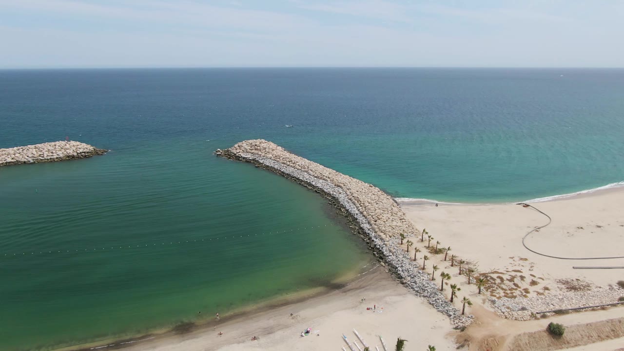 Aerial view of rocky breakwaters extending from a sandy beach into calm ocean.