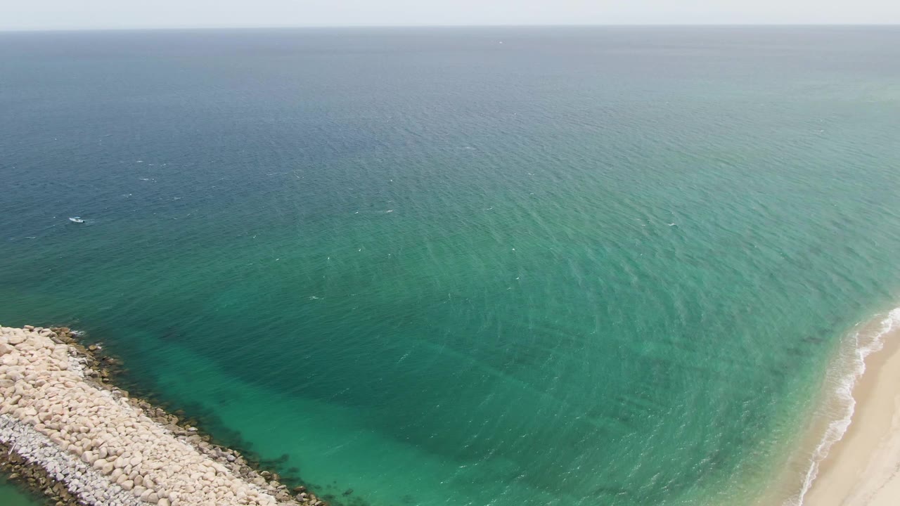Rock breakwater point bordered by clear turquoise water and a thin sandy beach.