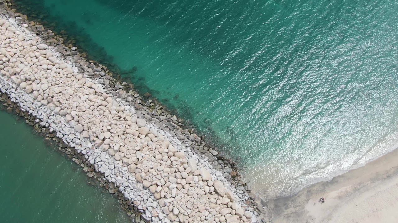 Rock breakwater dividing green-blue water from a sandy shoreline