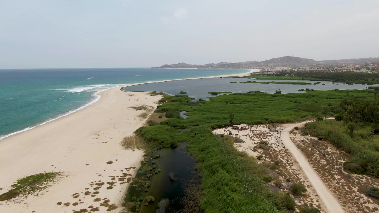 High coastal view with empty sand, ocean waves, lagoon, and green wetland vegetation.
