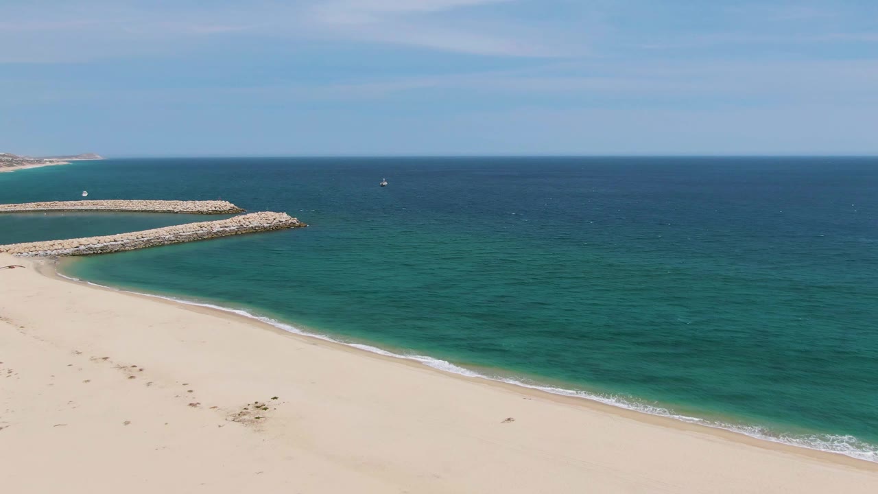 Wide aerial beach view with turquoise water and a rocky breakwater.