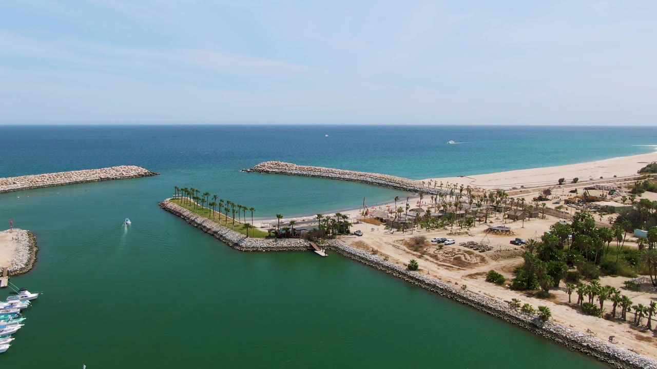 Aerial view of a boat wake inside a harbor entrance near rock breakwaters and beach.