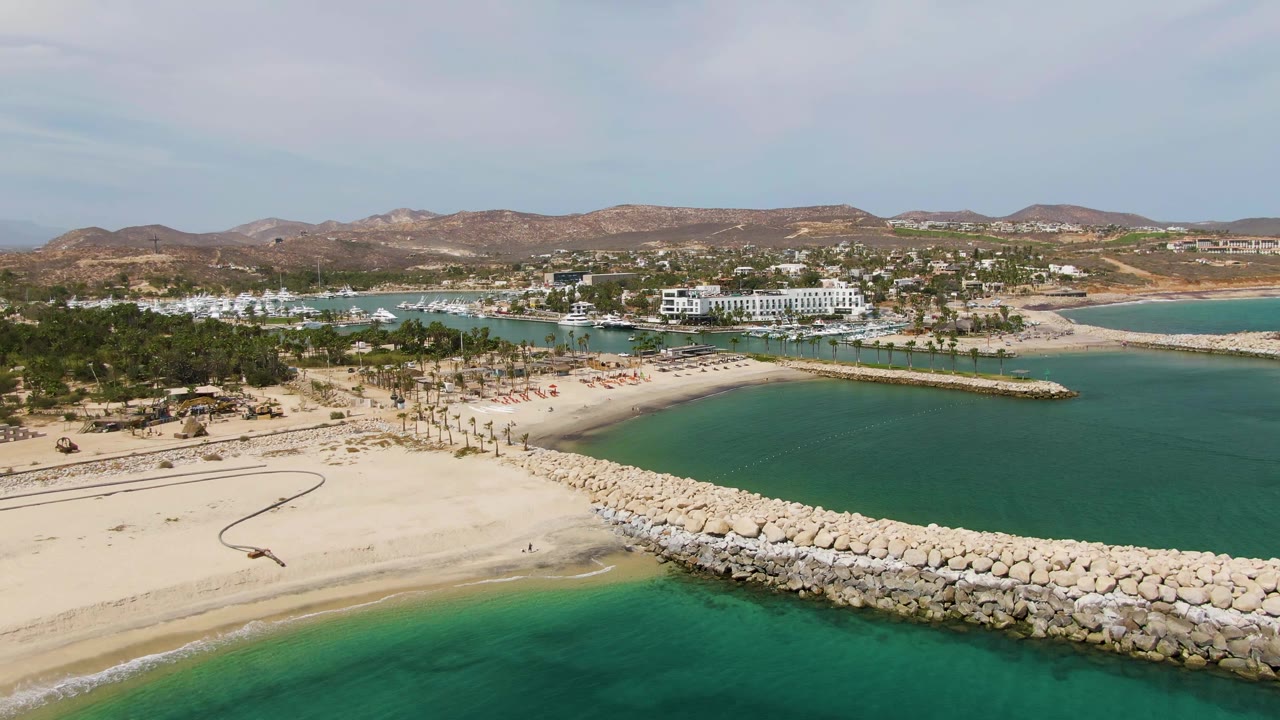 Beach and breakwater seen from above with calm ocean water and hills in the background.