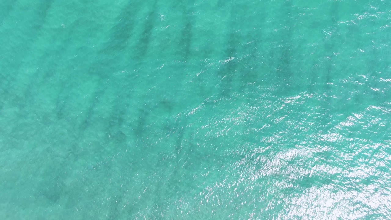 Clear blue-green ocean surface at Puerto Los Cabos Beach with small wavelets, brighter sun glints across the center, and no visible people.