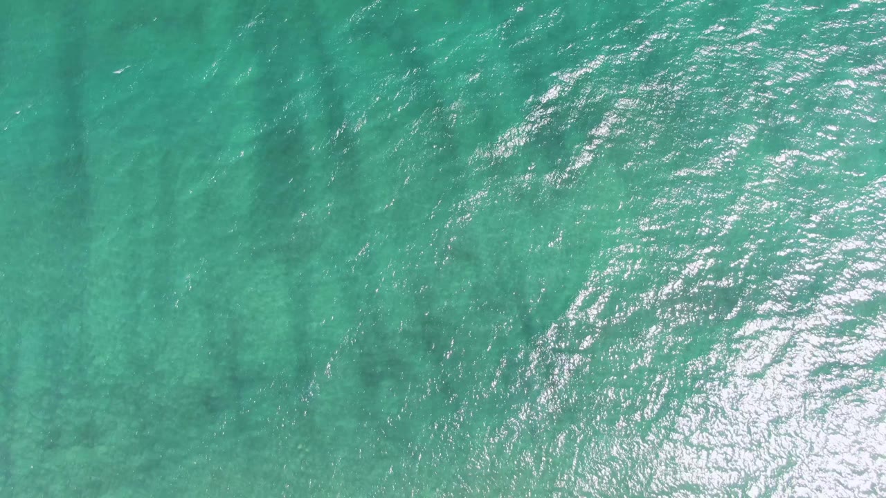Turquoise ocean surface with ripples and bright sunlight reflection.