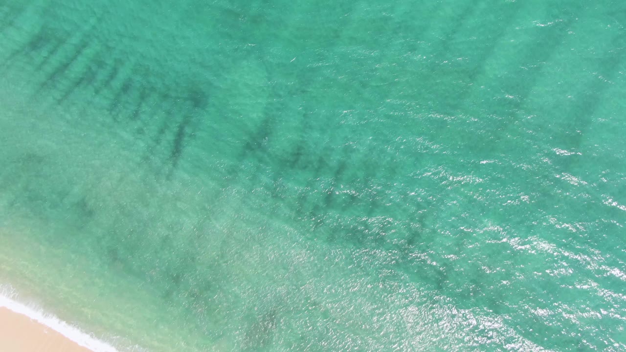 A small wave curls onto pale sand beneath turquoise water.