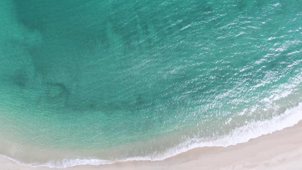 Overhead turquoise water washing onto pale sandy beach