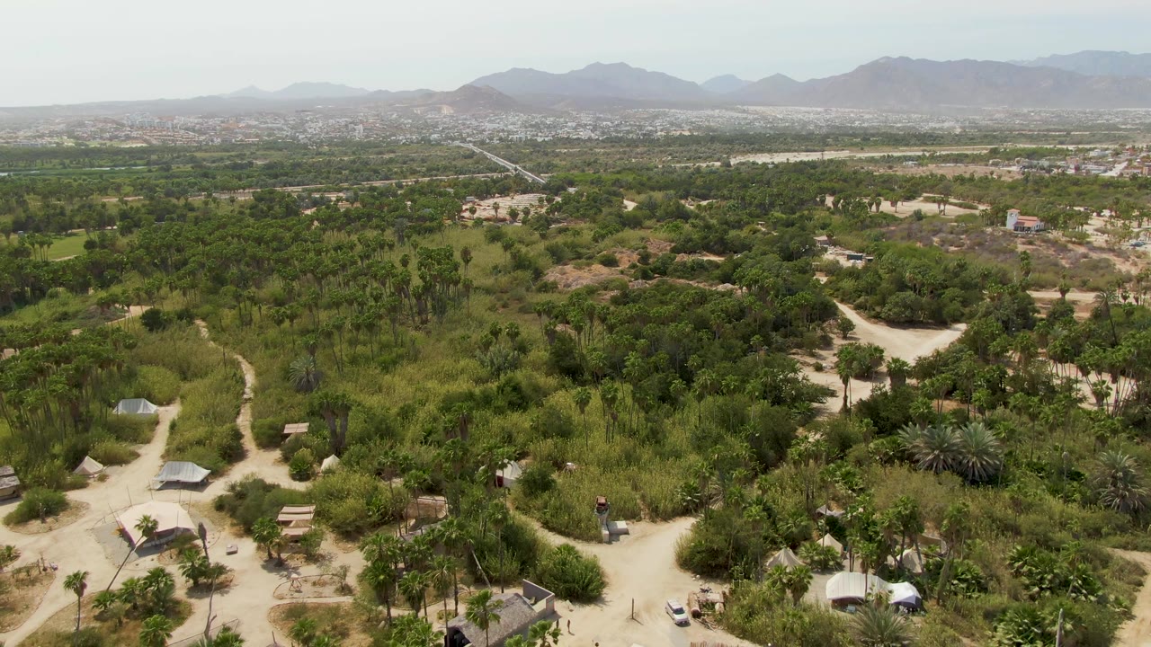 Wide aerial view of rural roads, vegetation, scattered rooftops, and mountains.