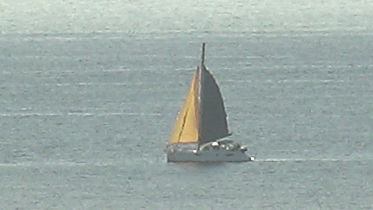 The sailboat has progressed to the right side of the open-water frame in Cabo Pulmo, Baja California Sur, with low glare on the ocean surface and no visible people.