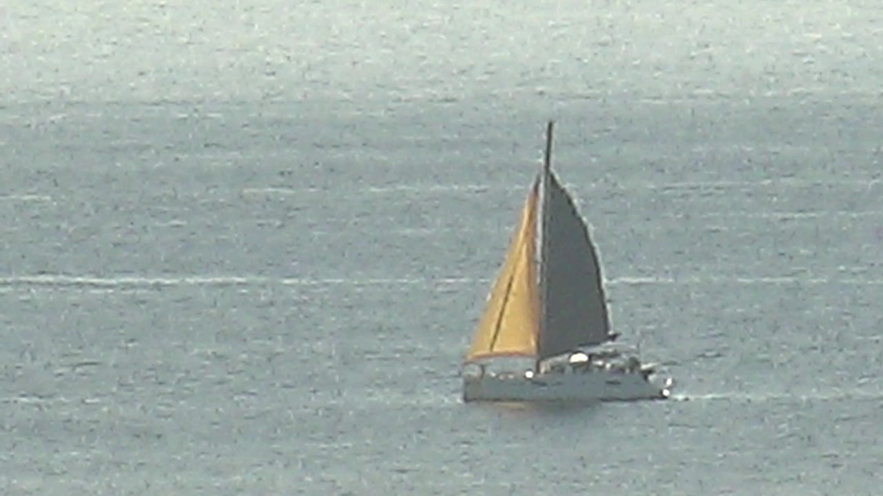 The sailboat sits slightly farther across the frame on calm water in Cabo Pulmo, with the yellow sail lit on one side and no visible people.