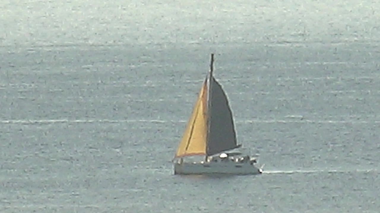 Sailboat with yellow and dark sails on calm ocean water.