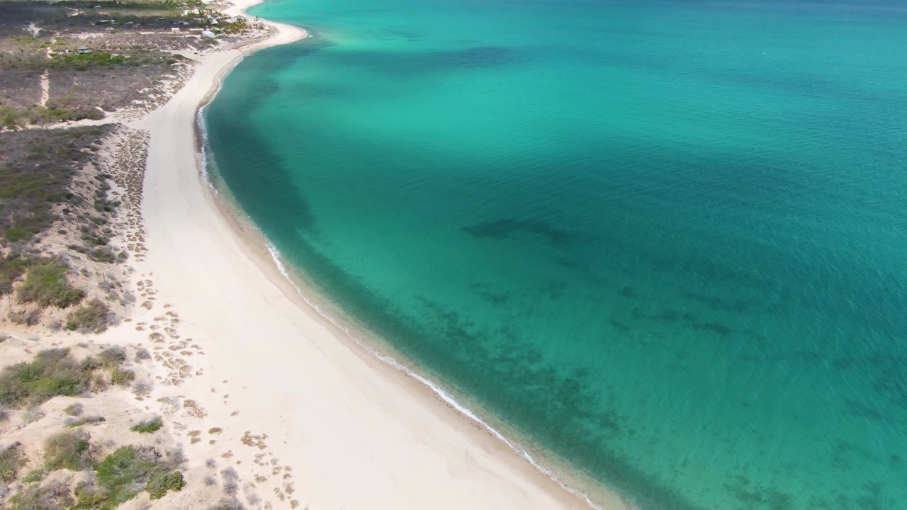 Aerial view of a curved white sand beach beside turquoise water.