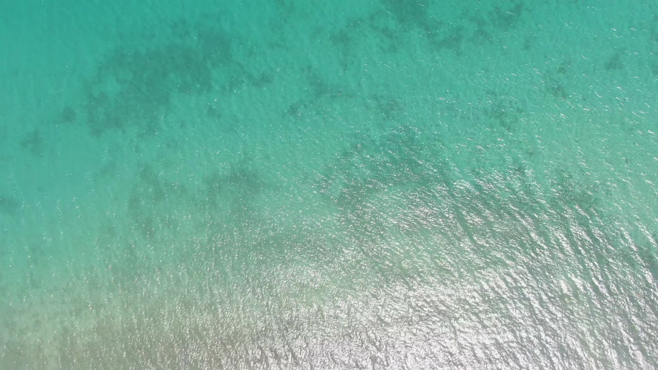 Top-down view of shallow turquoise water at Barakas Beach with pale seabed visible below ripples and no visible people.