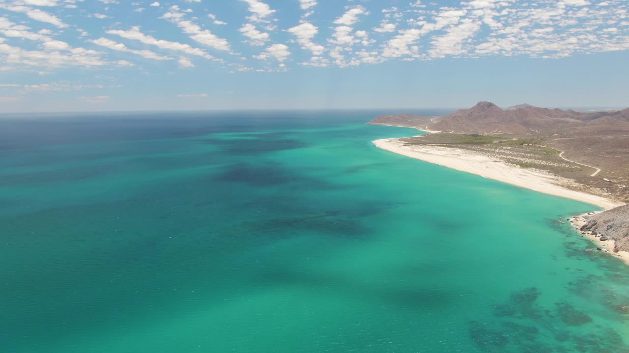 Turquoise water fills the frame with a sandy beach and mountains along the right side.