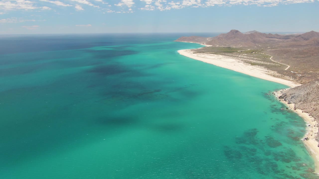 Aerial view of turquoise water beside a curving sandy beach and rocky coast.