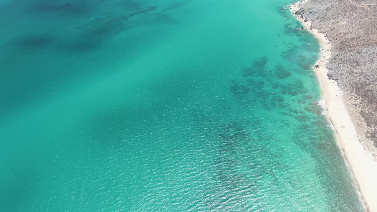 Aerial frame over Barakas Beach, Baja California Sur, with turquoise water filling the left side and a pale sand strip along the right edge.