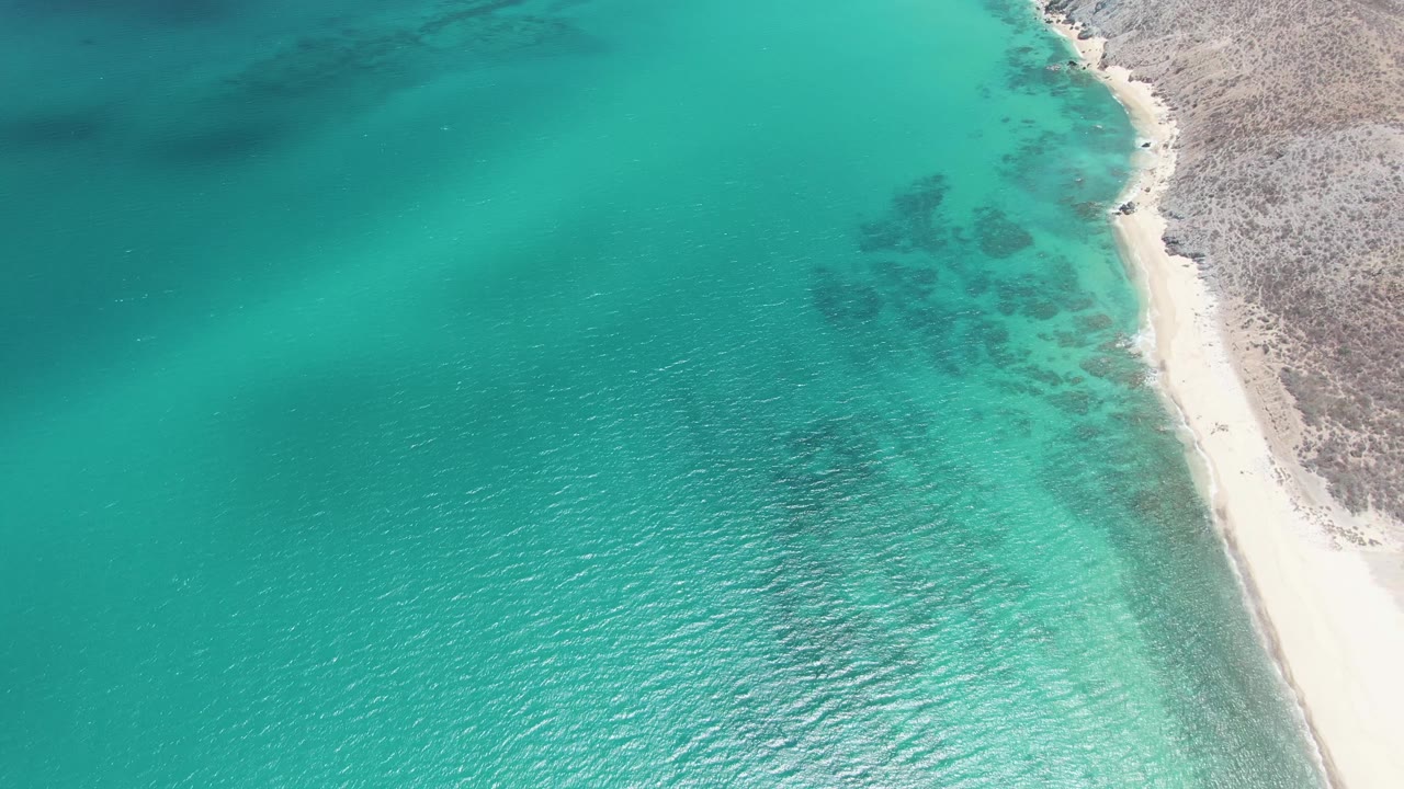 Aerial view at Barakas Beach, Baja California Sur, with the shoreline shifted slightly right and rippled turquoise water covering most of the frame.