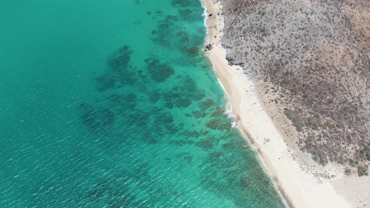 Turquoise shallows and dark reef patches border a narrow white sand shoreline.