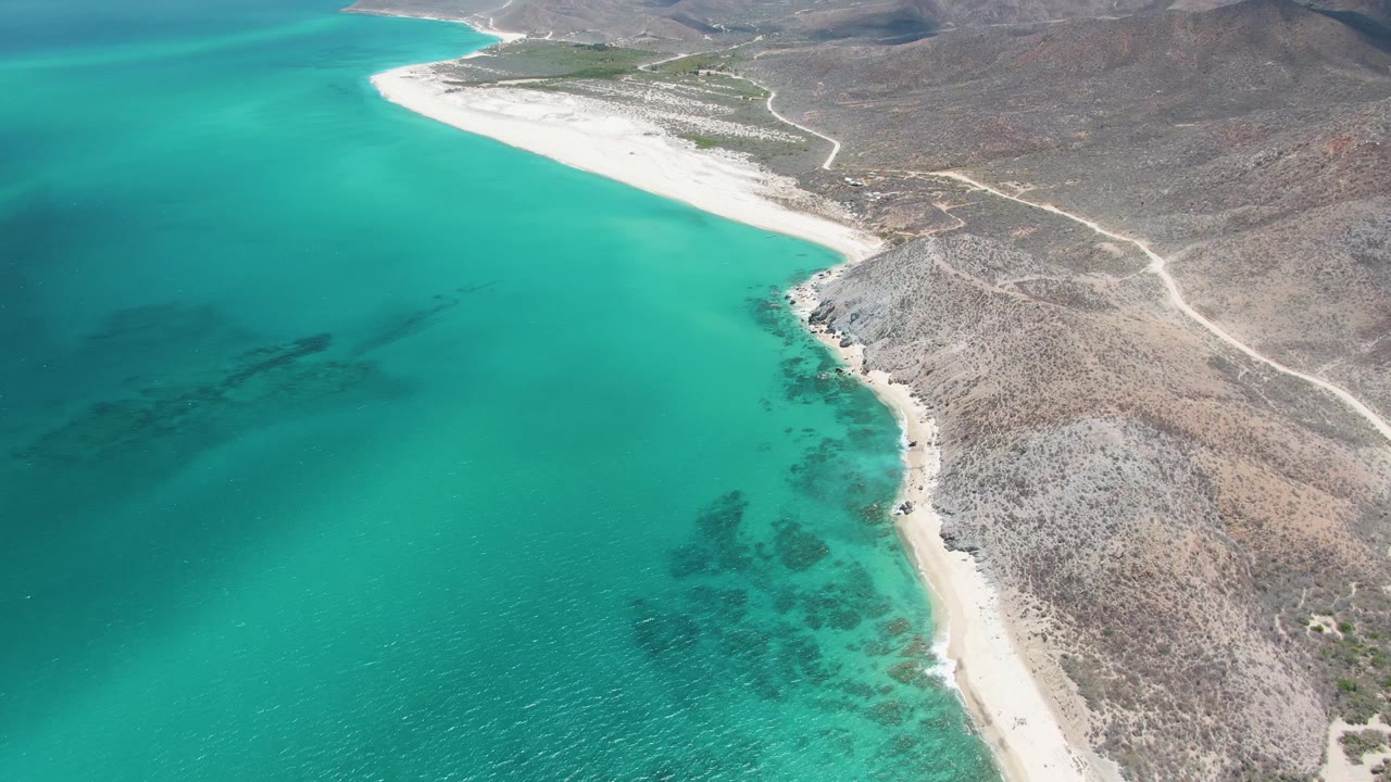 Turquoise bay water beside a narrow beach and rocky slope.