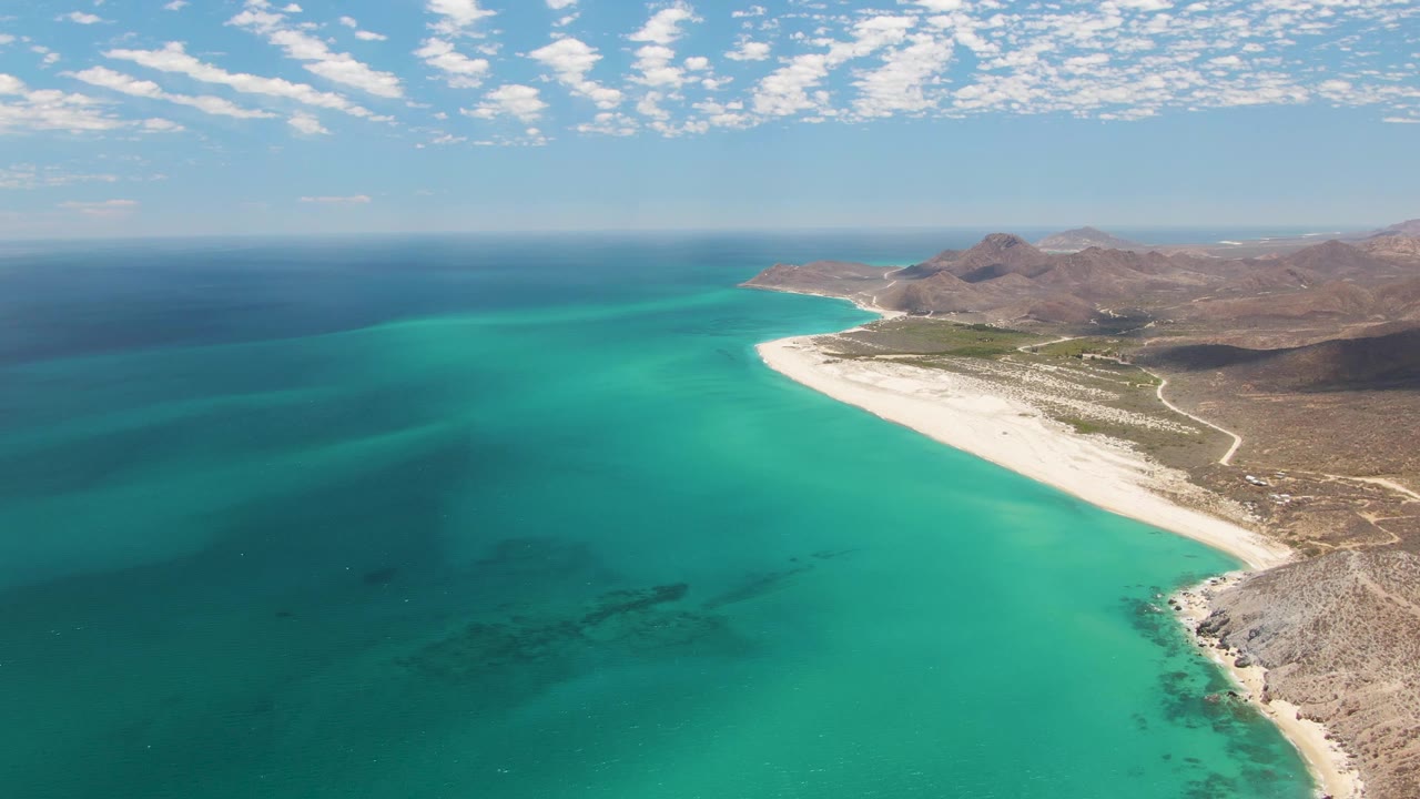 Wide aerial beach scene with turquoise sea, white sand, and low clouds.