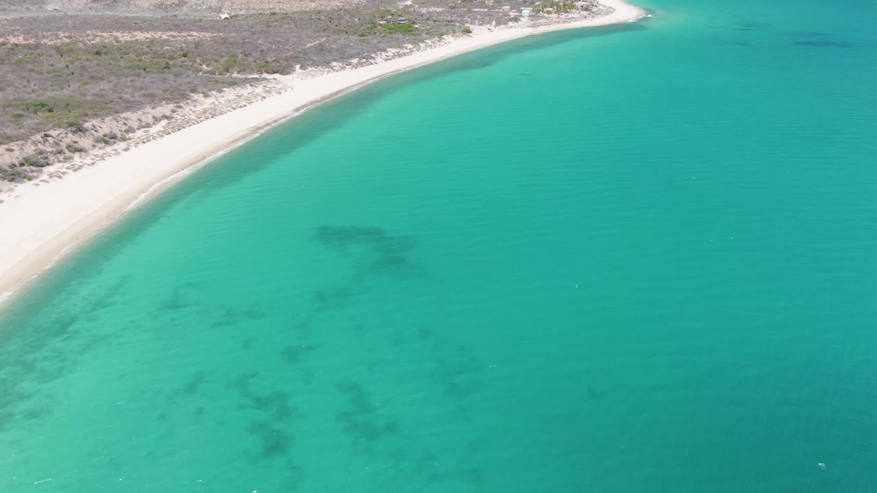 Drone view of white sand beach beside clear turquoise water.
