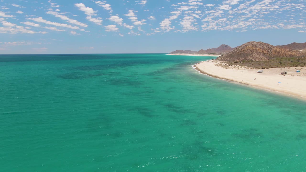 Turquoise ocean stretches toward a sandy shoreline with low rocky hills behind it.