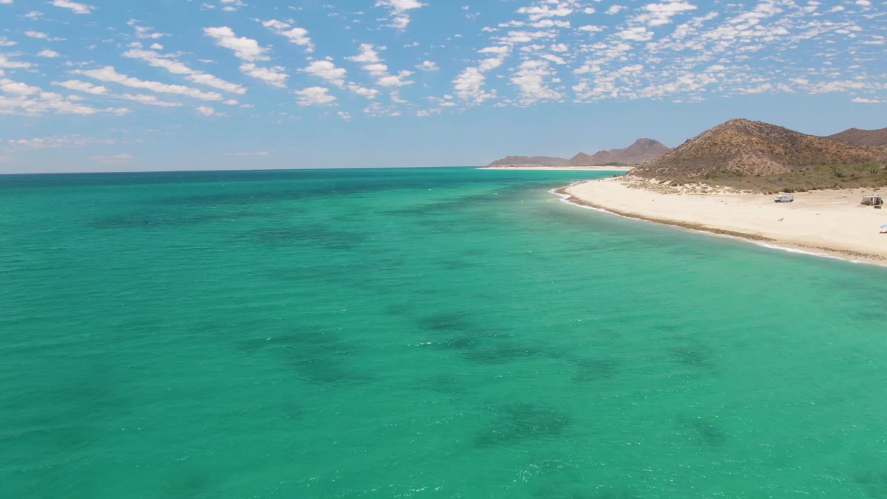 Turquoise ocean beside a white sand beach and low hills.