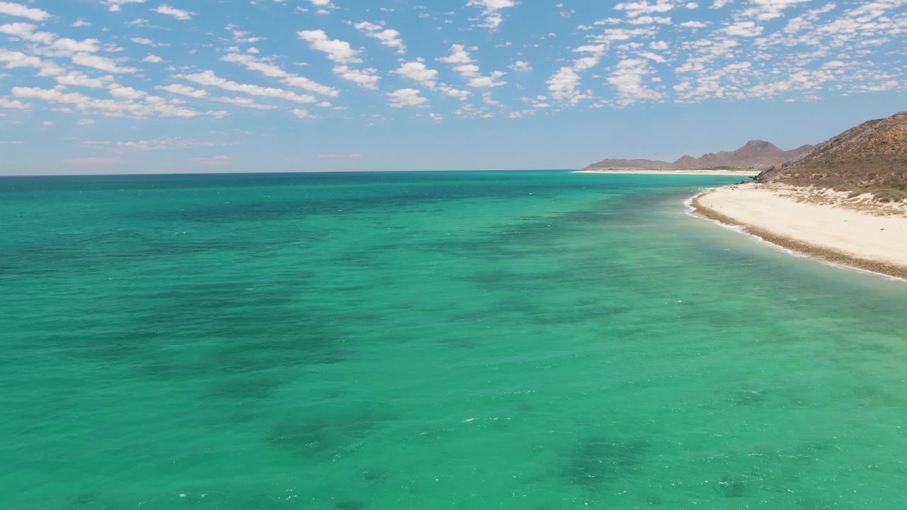 Wide turquoise ocean with white beach and distant hills