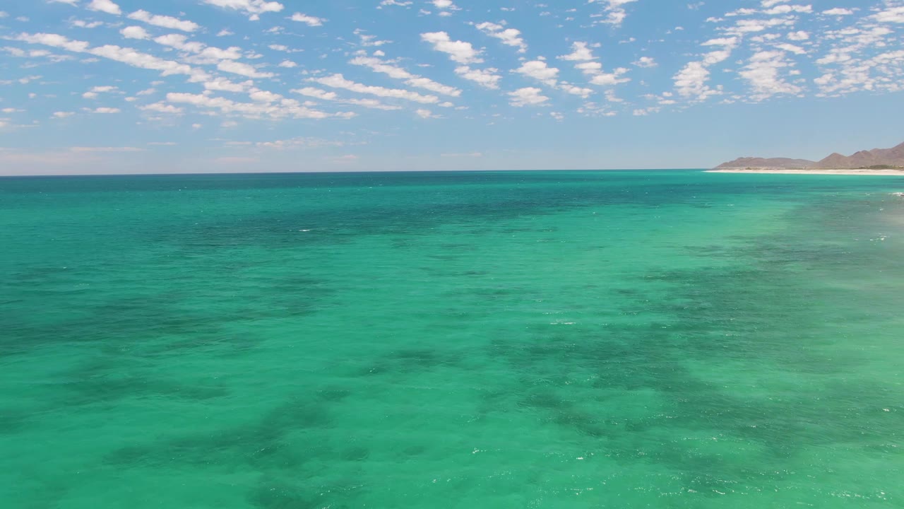 Turquoise ocean under scattered clouds with distant beach and land