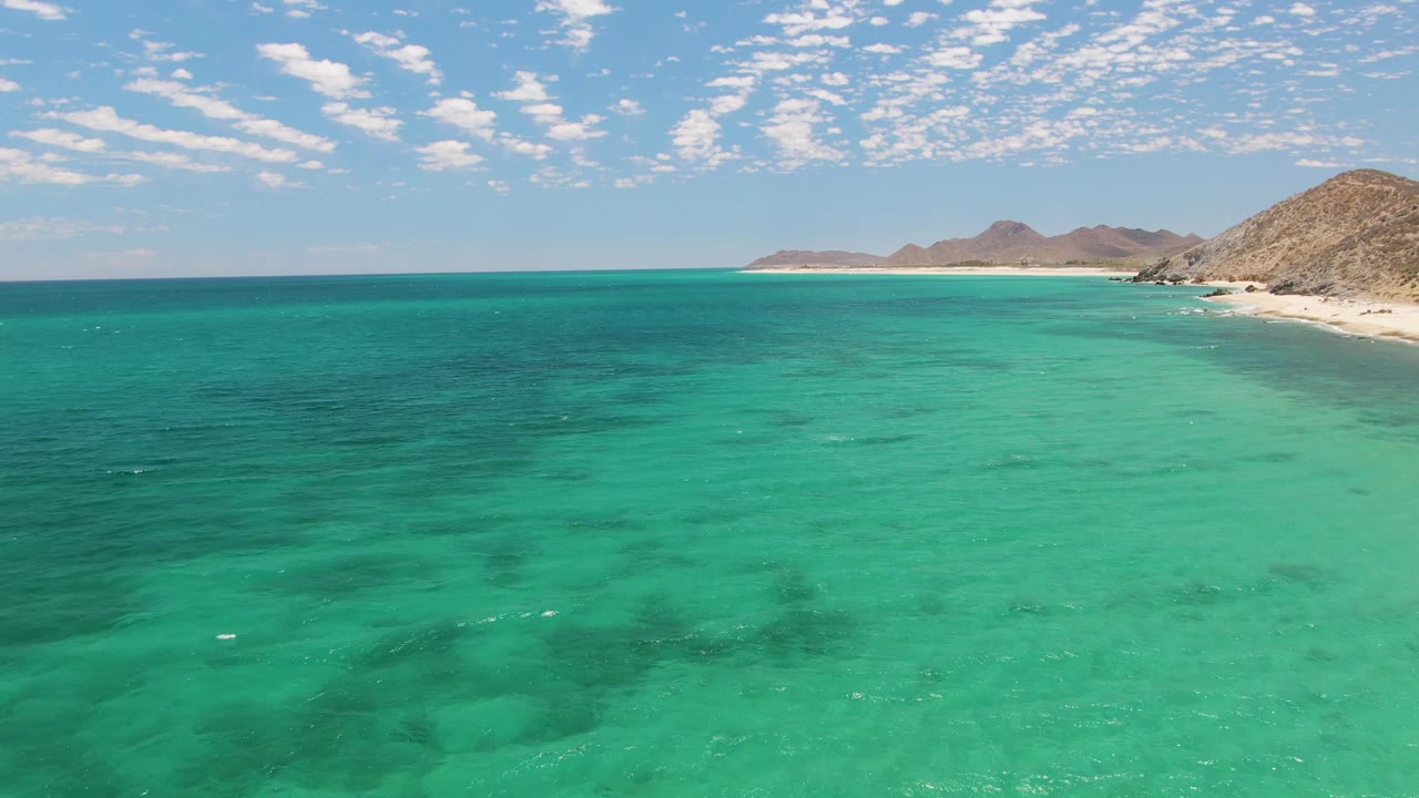 At two seconds, darker patches under the turquoise water are visible near the center, with the Barakas Beach shoreline and dry hills to the right and no visible people.