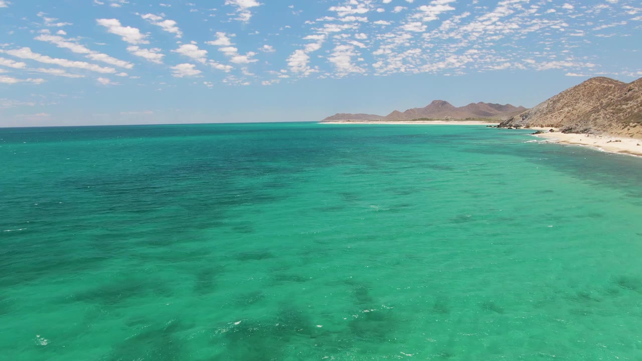 At three seconds, the aerial view shows more of the pale Barakas Beach shoreline stretching across the right side, with turquoise water in front and no visible people.