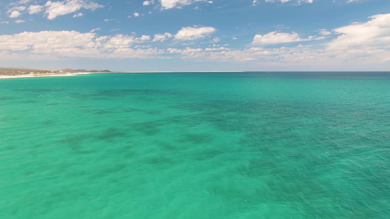 At 0:01, the Barakas Beach shoreline remains on the left edge while clear turquoise water and soft cloud cover dominate the frame, with no visible people.
