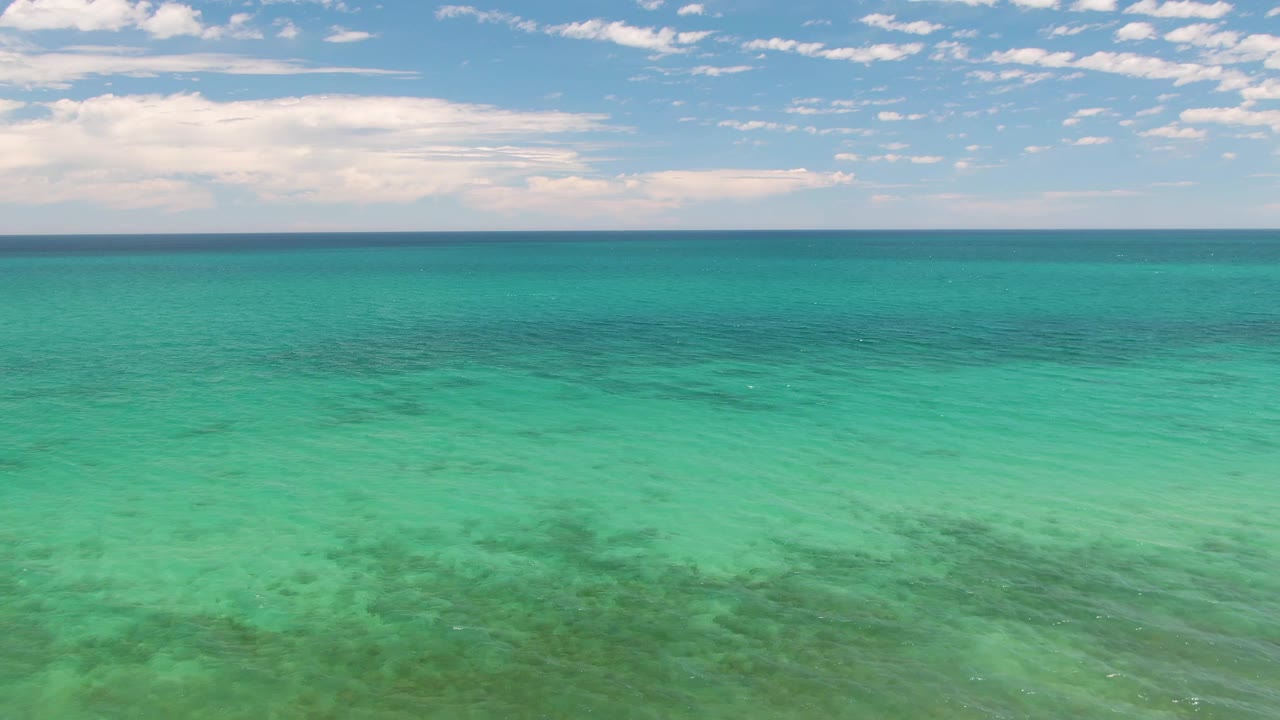 Clear green-blue ocean surface with seabed texture and cloudy sky.