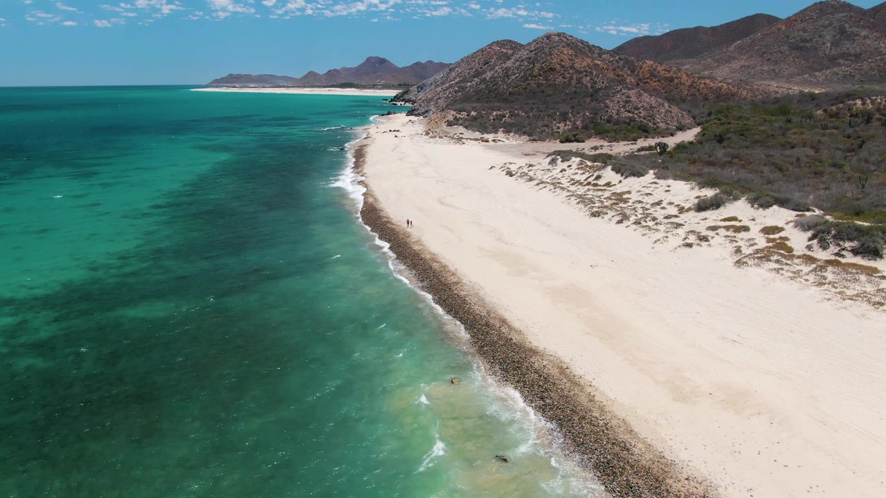 Aerial view of turquoise ocean beside a pale sandy beach and rocky mountains