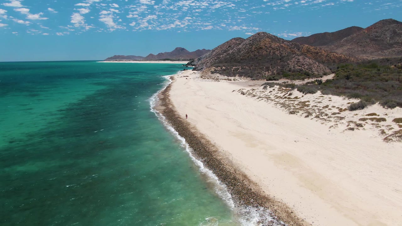 Turquoise water and curved sandy shoreline below rocky hills.