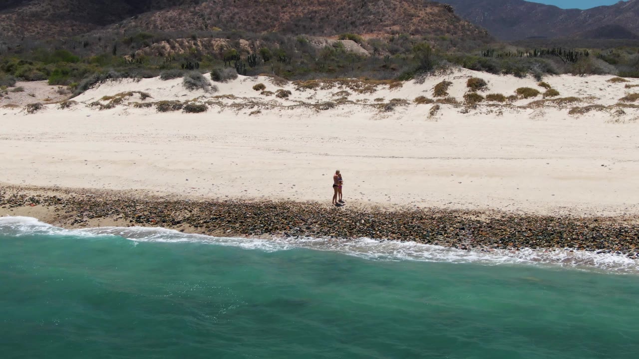 Person walking along rocks between surf and wide sandy beach.