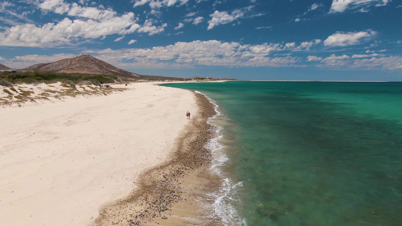 Curving sandy shoreline with turquoise ocean and small walkers by the surf.